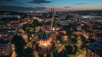 Stunning evening view of Gotheborg, Sweden showcasing city lights and historic architecture. Flying around Oscar Fredriks Church in Gotheborg with citylights and red sunset sky