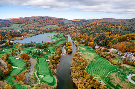 Aerial view of the Connecticut River snaking through a vibrant tapestry of fall foliage near a golf course and lake, White River Junction, Vermont, United States.