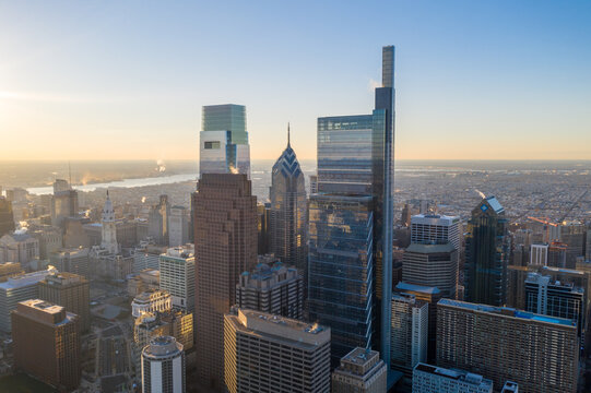 Aerial view of skyscrapers piercing the sky, their glass facades reflecting the warm hues of the setting sun over the city skyline, Philadelphia, Pennsylvania, United States.