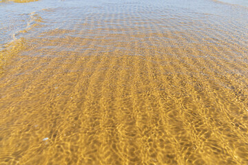 Intricate sand ripples visible beneath clear, shallow water with gentle waves, at the serene coast of the Baltic Sea, creating natural abstract patterns