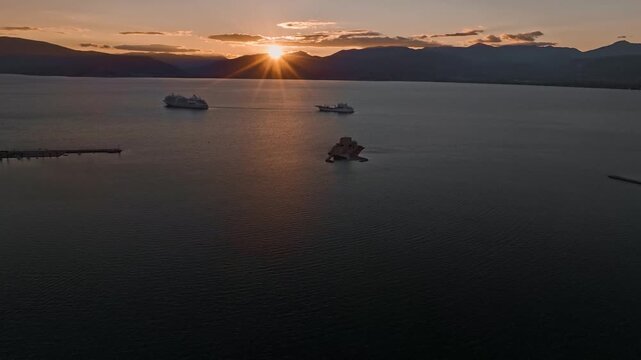 Aerial view of the Bourtzi castle and ships on calm waters reflecting the golden sunset, creating a serene scene, Nafplion, Argolis, Greece.