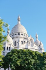 Domes of Basilica of Sacred Heart of Montmartre known as Sacré-Cœur Basilica in Paris, France, surrounded by green trees against the blue clear sky. Traveling and sightseeing spots, vacation in Europe