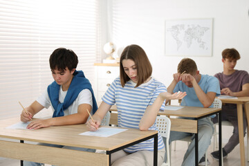Students taking exam at wooden table indoors