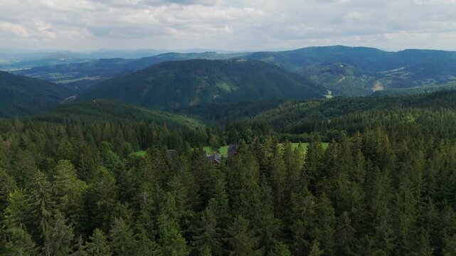 Aerial view of houses nestled among dense green trees, with mountains rising in the background under a cloudy sky, Jablunkov, Moravian-Silesian Region, Czechia.