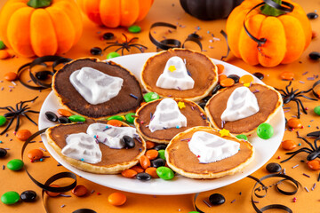 Tasty Halloween pancakes topped with marshmallow ghosts. Halloween morning dessert, for breakfast or brunch, with colorful candies, sweets and Halloween decorations