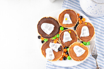 Tasty Halloween pancakes topped with marshmallow ghosts. Halloween morning dessert, for breakfast or brunch, with colorful candies, sweets and Halloween decorations