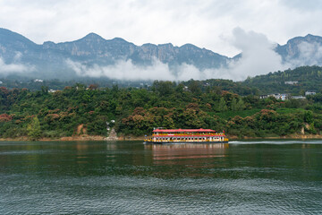 A large boat travels along a wide river with green forested hills and misty mountains in the...
