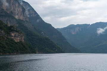 Enshi City, China mountains rise above the wide river water on a cloudy day presenting a majestic...