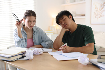 Tired students with books preparing for exam at wooden table indoors