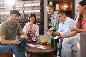 Group of friends playing cards at wooden table indoors