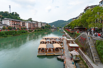 boats float river water buildings line shore with trees green water，Xuan'en County, Enshi Tujia...
