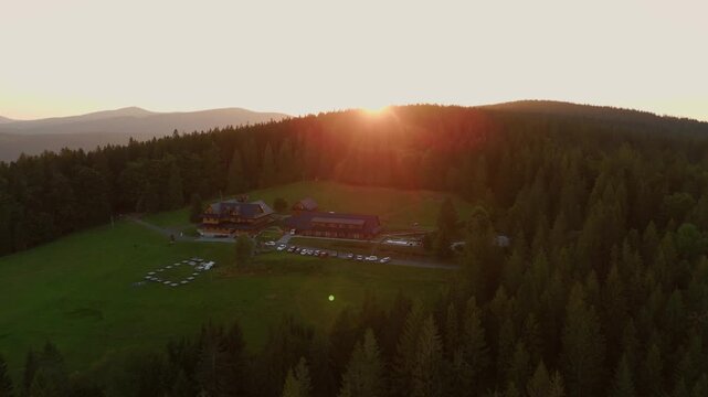 Aerial view of buildings surrounded by a dense forest, the golden sunlight contrasting with the verdant trees, Jablunkov, Moravian-Silesian Region, Czechia.