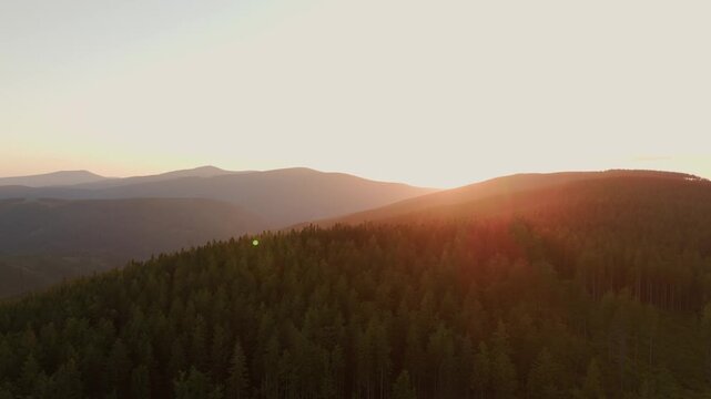 Aerial view of a golden sunset over the dense forest and distant mountains, creating a stunning contrast of light and shadow, Jablunkov, Moravian-Silesian Region, Czechia.
