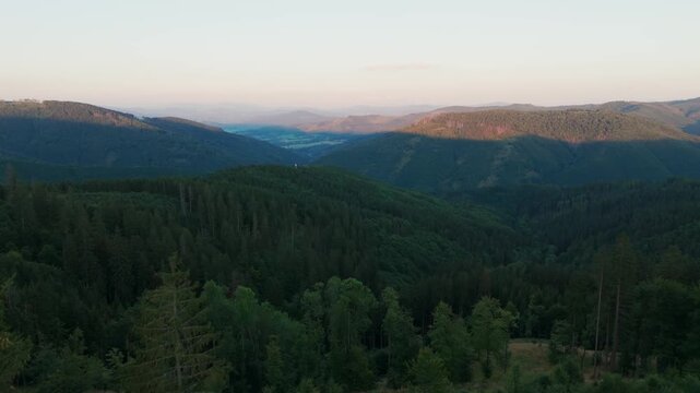 Aerial view of forested hills casting dark shadows, with the distant hills fading into a soft blue haze, Jablunkov, Moravian-Silesian Region, Czechia.