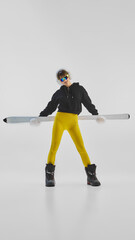 Obraz premium Young woman in bright winter outfit holding skis horizontally with attitude. Concept of influencer winter fashion, confidence, and bold expression for social media, lifestyle, and athleisure branding.