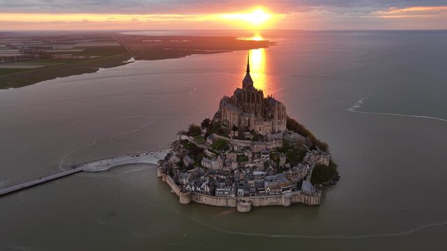Aerial view of the majestic Mont Saint-Michel and its causeway under a radiant sunset, casting a golden glow on the water, Mont Saint-Michel, Normandy, France.