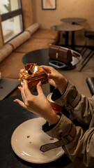 Girl enjoying a pastry in a cafe setting, showcasing fashion and lifestyle.