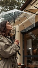 Fototapeta premium Girl in trench coat under a clear umbrella on a rainy day
