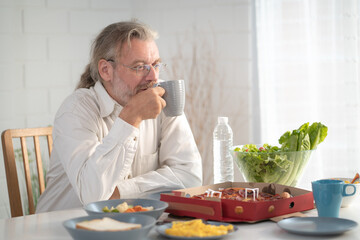 Senior elderly older grandfather stay at home with painful face sitting alone on eating table in house. Depressed elderly retired man upset feeling unhappy. Lonely and missing his family at home	