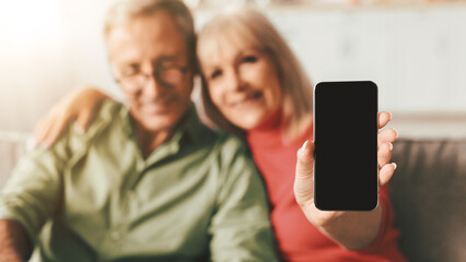 Senior Couple Showing Smartphone With Blank Screen To Camera Advertising New Application Hugging...