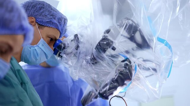 Focused male Caucasian surgeon looks at microscope binocular. Side view portrait of a doctor performing modern neurosurgery.