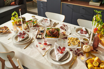 Thanksgiving table setting featuring roasted turkey, assorted vegetables, fruits, candles, and decorative autumn leaves arranged for holiday meal, no people visible in scene