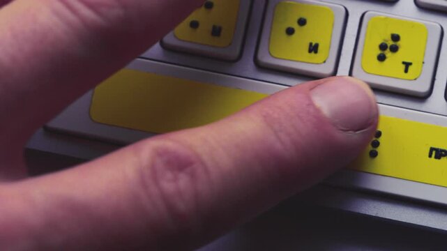 Computer keyboard with braille font alphabet. Blind person is typing words, hands. Technological device for visually impaired people. Tactilely touches bumps on keys. Inclusion, assistive technology