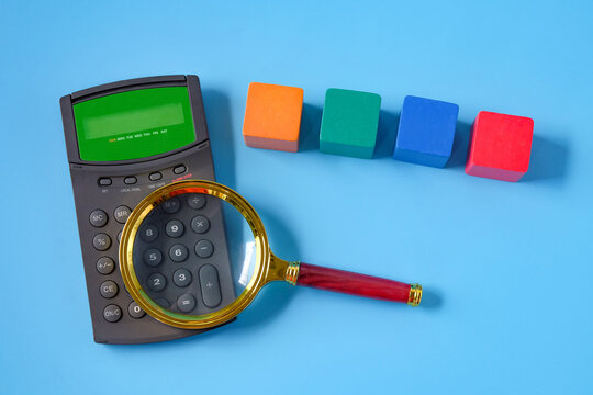 Magnifier glass with calculator and color wood cube. - Powered by Adobe