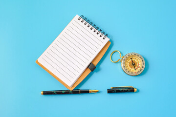 A fountain pen and a brass compass resting on notebook.