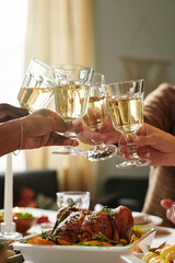 Diverse group of adult hands clinking wine glasses over Thanksgiving table, celebrating together with roasted poultry dish in foreground, capturing joyful moment of shared meal