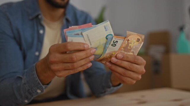 Man counting euro bills in a cozy living room interior, highlighting financial planning in a new home setting.