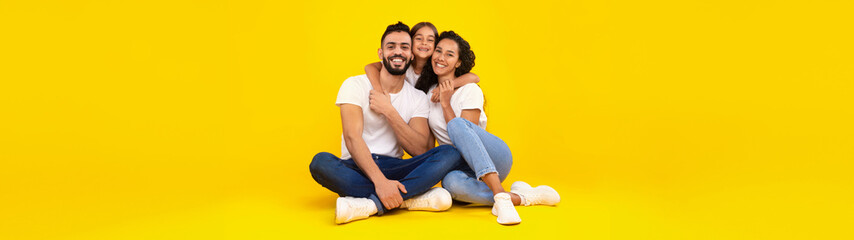 Obraz premium Arabic Parents And Little Daughter Hugging Posing Together Sitting On Yellow Background, Smiling To Camera. Studio Shot Of Arab Family Embracing Expressing Positive Emotions