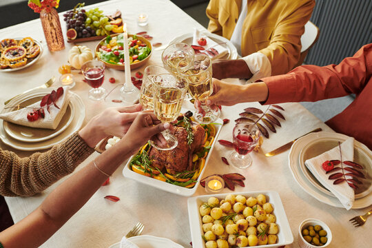 Diverse group of young adults and Young people clinking wine glasses over Thanksgiving dinner table, celebrating together with roasted turkey, potatoes, salad and fruit visible