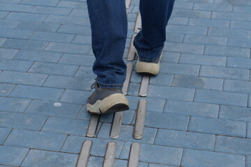 Feet Walking on Tactile Guiding Strips: Close-up of Accessibility Paving