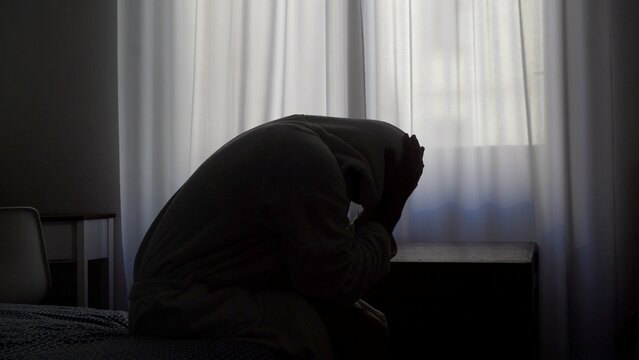 Depressed  man sitting on bed holding head grief pain crisis separation fatigue headache burnout bedroom guy male emotional stress tired exhaustion sadness anxiety distraught problems overworked loss