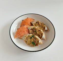 A close-up view of stuffed crab shells filled with a flavorful spiced crab mixture, garnished with herbs and chili, served in a white bowl with a black rim on a clean white background.