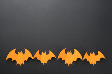 Halloween decor. Orange paper bats on black background, flat lay. Space for text