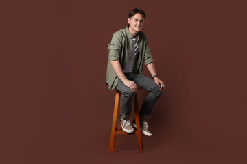 Man in stylish jeans on stool against brown background