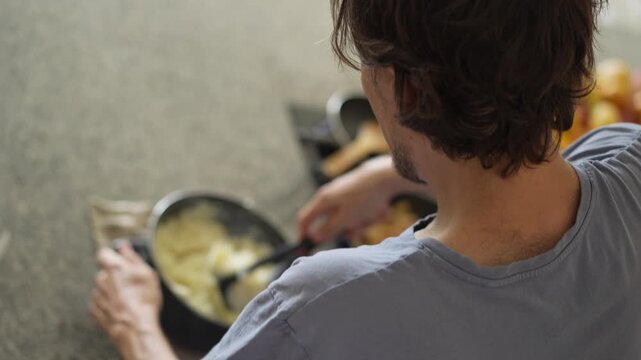 A young man is cooking food in the kitchen, focusing on preparing a delicious homemade meal. A relatable and warm moment of homemaking, creativity, and culinary enjoyment in a cozy setting.