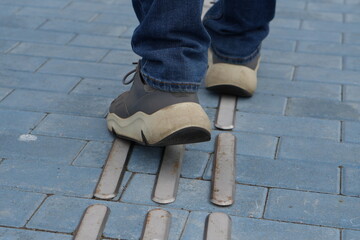 Feet Walking on Tactile Guiding Strips: Close-up of Accessibility Paving