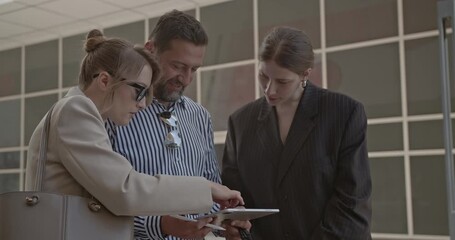 Diverse business team collaborating on a digital tablet during an outdoor meeting in a bustling city district. - Powered by Adobe