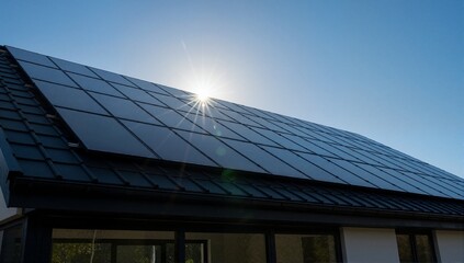 Naklejka premium Solar panels on the roof of a modern house with the sun shining brightly. Photovoltaic system for renewable green energy. Sustainable technology concept with copy space