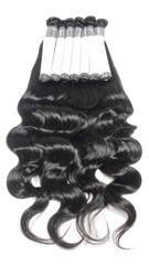 A close-up shot displays bundles of wavy, black hair extensions laid out, with some arranged atop other bundles. The background is clean and white