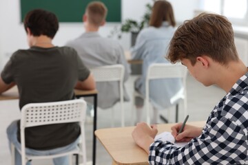 Students taking exam at wooden table indoors, selective focus