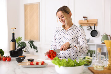 Cooking process. Smiling woman cutting bell pepper at table in kitchen