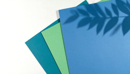 A close-up shot displays layered colored paper sheets, subtly shadowed by foliage, offering a vibrant and minimalist aesthetic