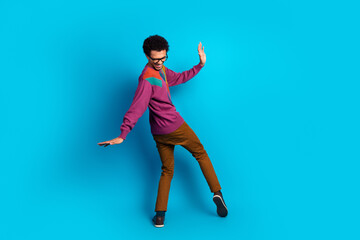 Trendy young man in colorful outfit posing playfully on vibrant blue background, expressing energy and a retro fashion vibe