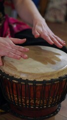 A close-up shot features a person's hands positioned on the drumhead, about to create rhythmic music with wooden instrument