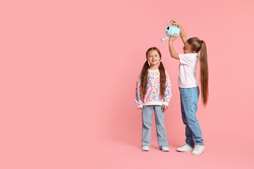 Little girl holding watering can above her friend on pink background, space for text. Grow up faster