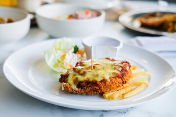 A serving of crispy chicken parmigiana or schnitzel topped with melted cheese, served with french fries and a salad on a white plate